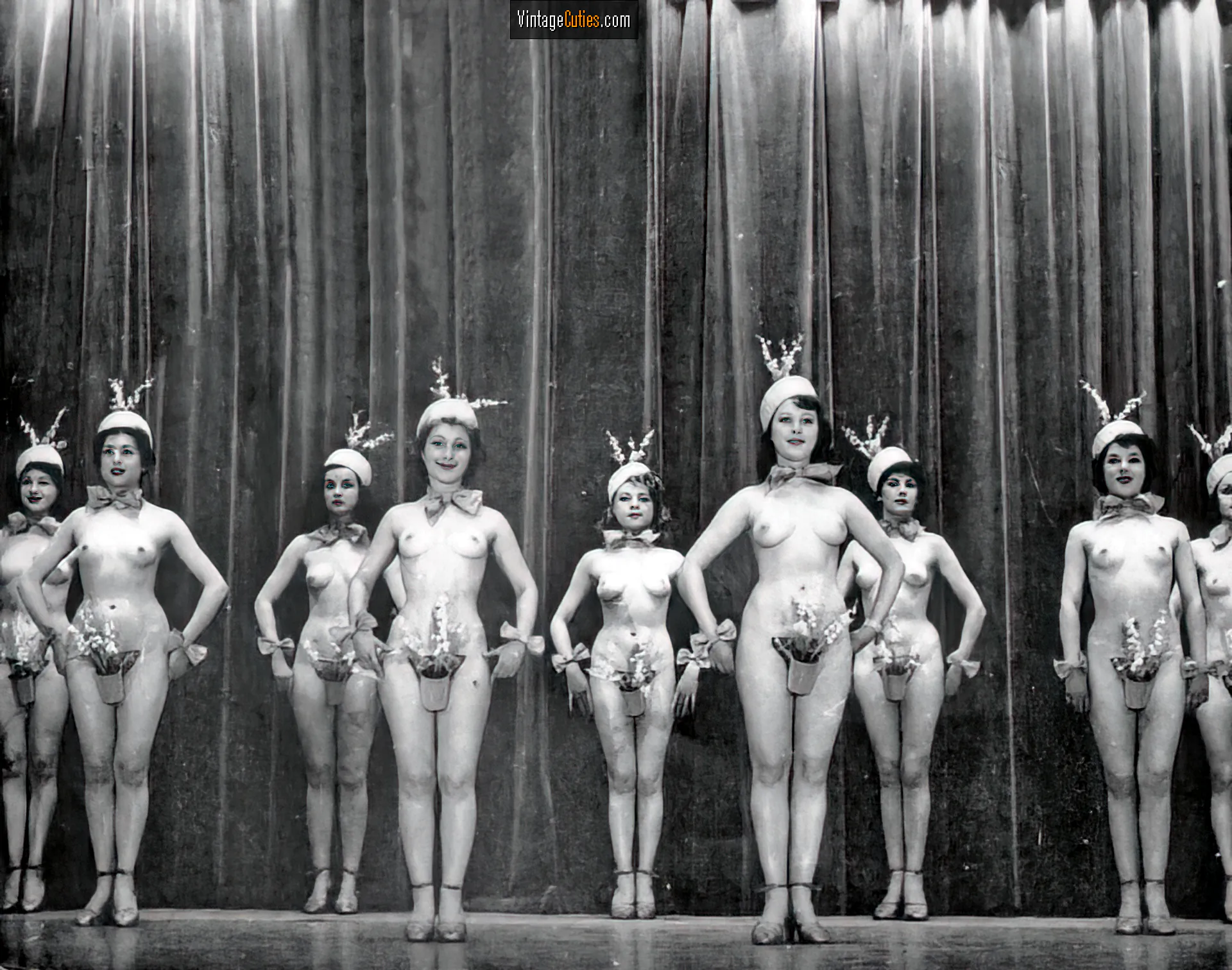 Burlesque girls stand topless on the stage with their pussies covered